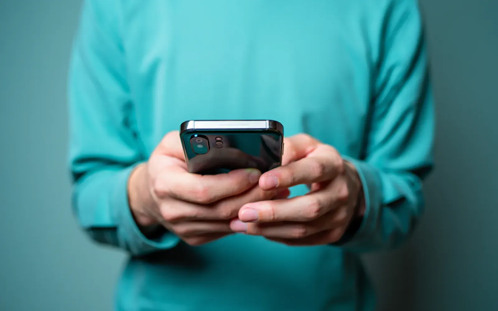 A person in a teal sweater holding a smartphone with both hands, testing a website on a small screen.